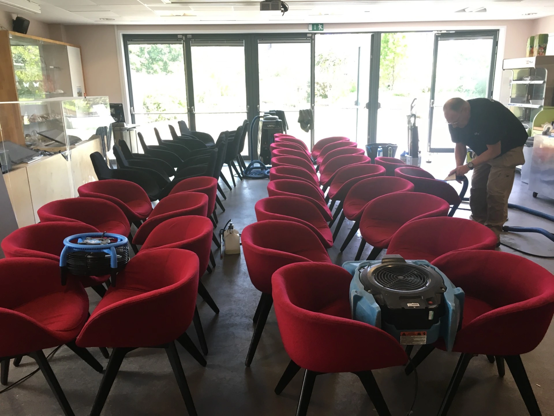 A large function room with red chairs and a person cleaning them with upholstery cleaning machine