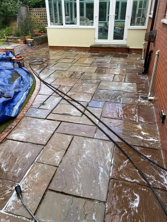 Patio being pressure washed with soap and water, showing hose and wand.