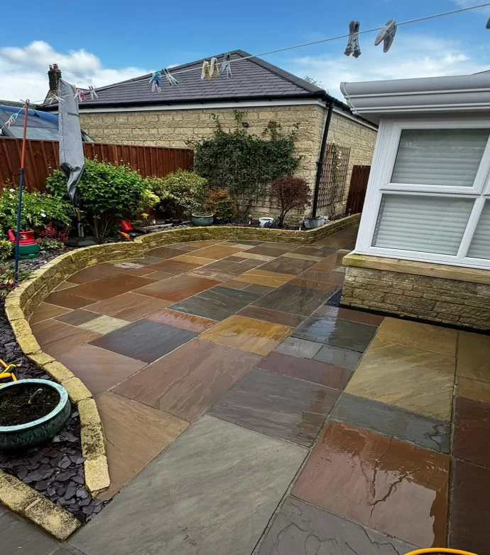 Clean, wet multi-coloured flagstone patio with surrounding garden.