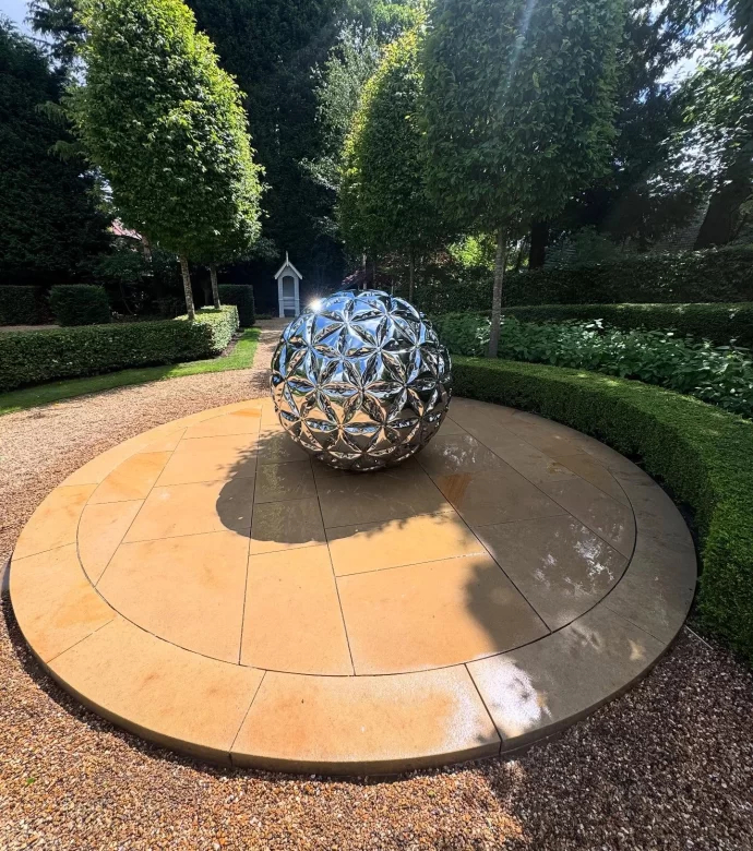 Decorative circular patio that has just been washed, with metallic spherical sculpture on surface.