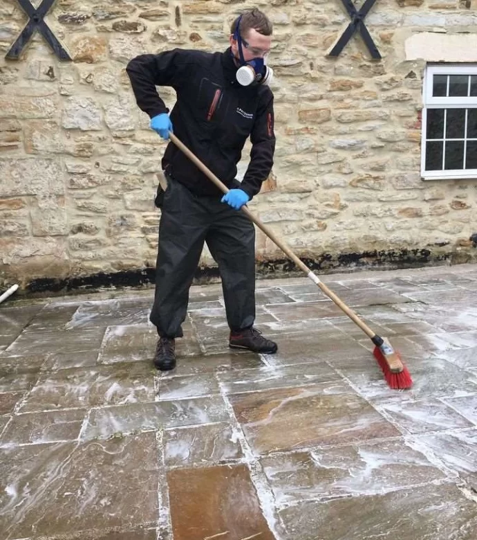 Member of the Paul Dyson team using a brush to clean large patio.