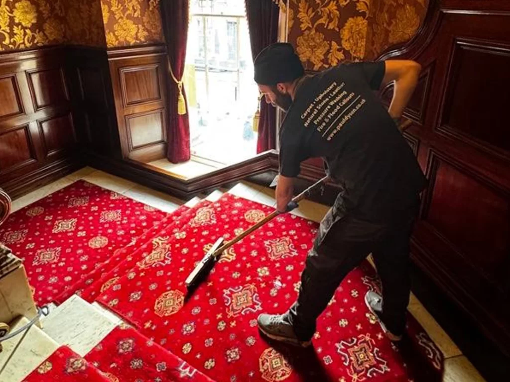 Elegant red carpet in hotel being hoovered by professional carpet cleaners.