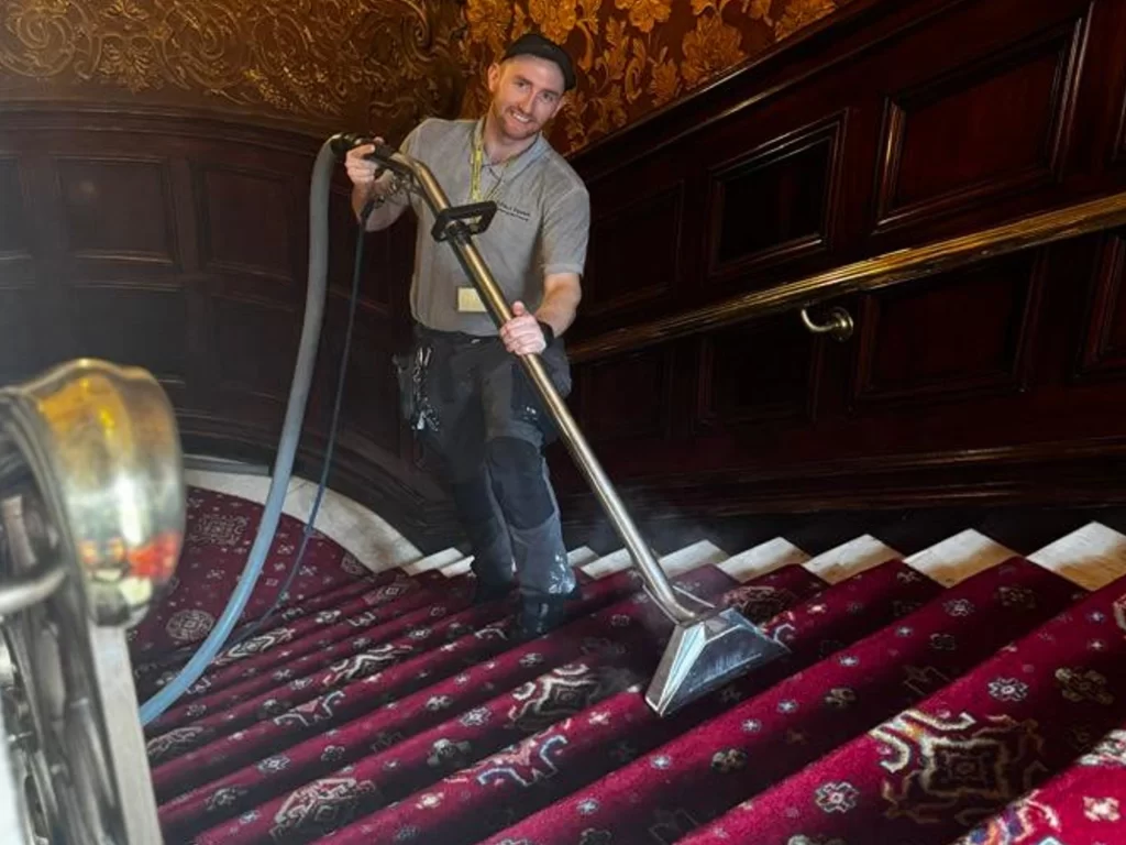 Professional carpet cleaners vacuuming red carpeted stairs in hotel.