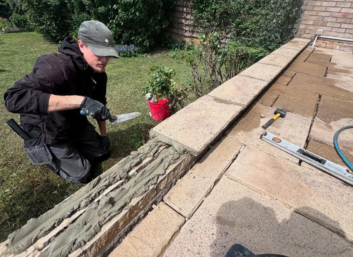 Paul Dyson employee applies fresh mortar into the joints of a stone patio edge for repointing.