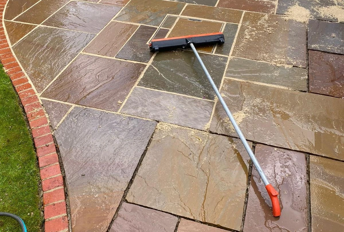 A long-handled brush on a stone patio.