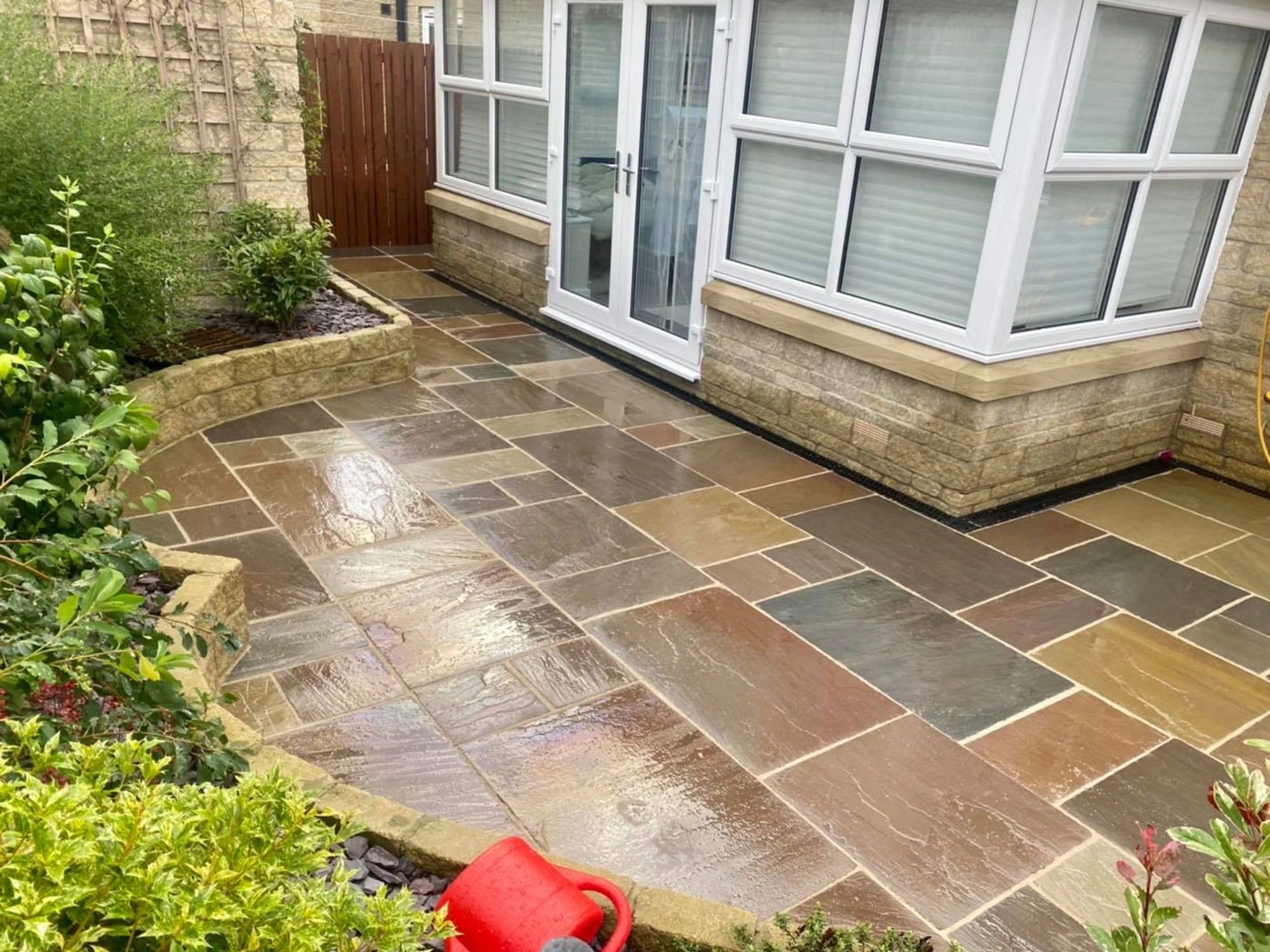 A clean, multi-coloured Indian sandstone patio with a vibrant wet-look finish, wrapping around a white conservatory.