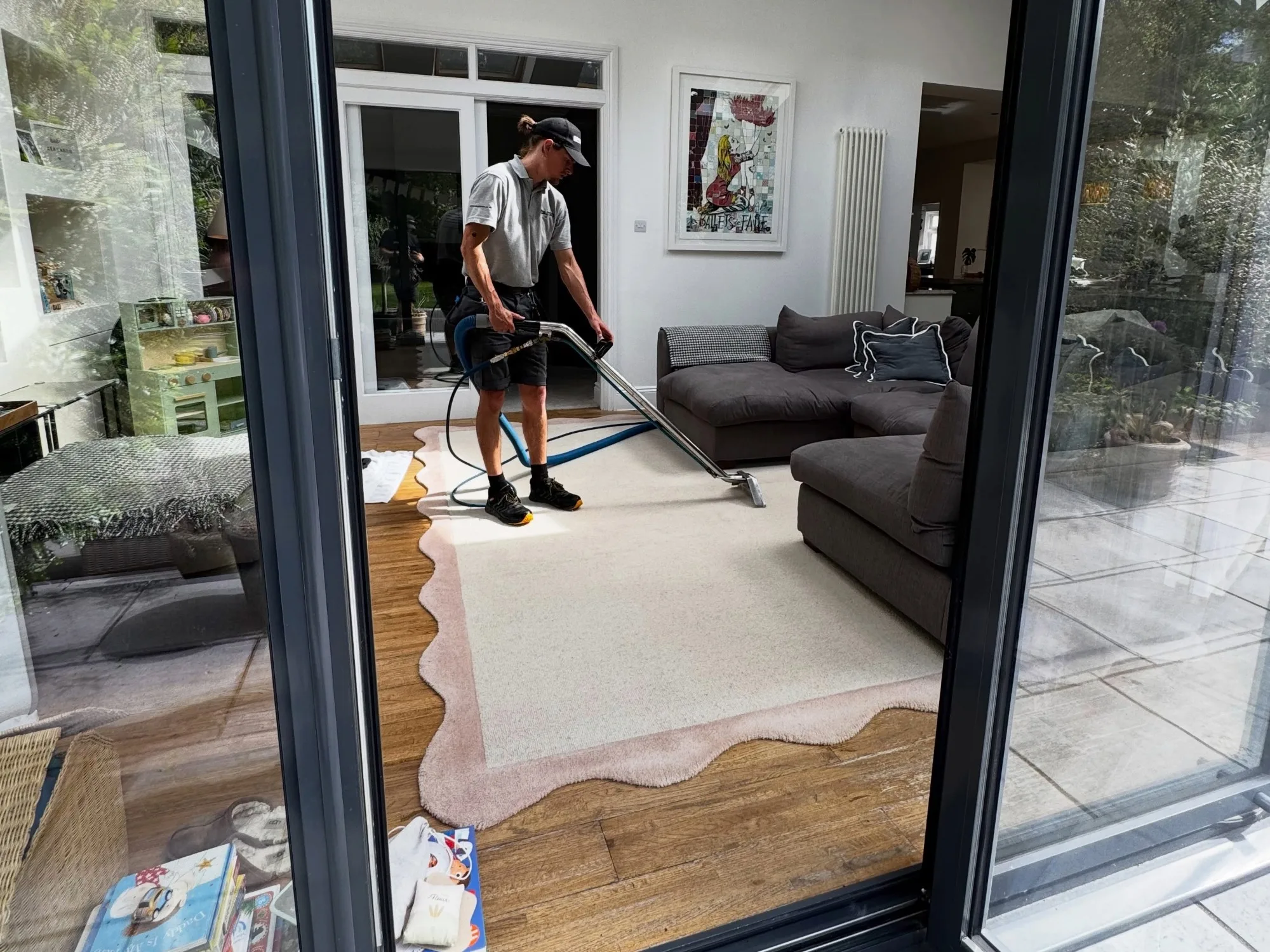 A member of the Paul Dyson team cleaning a large rug in a family living room with the glass door open.