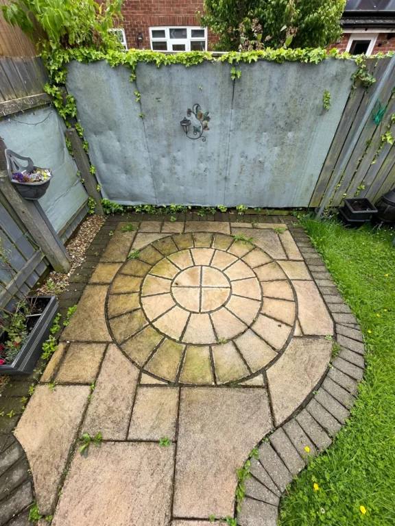 A decorative sandstone patio with weeds sprouting from cracks in the old, crumbling pointing.