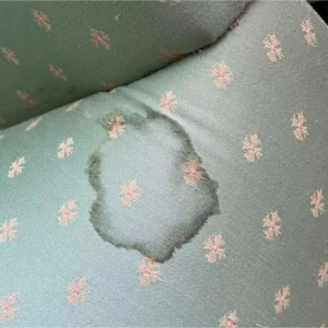 A pale blue patterned sofa with a large ringed stain on its side.