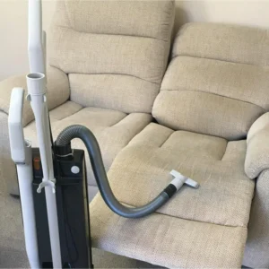 A cream, linen sofa after being thoroughly vacuum-dried professionally, with the vacuum in front of it.